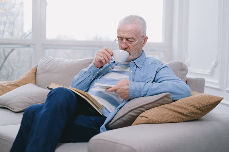 An Elderly Man With Eyeglasses Drinking From A White Cup