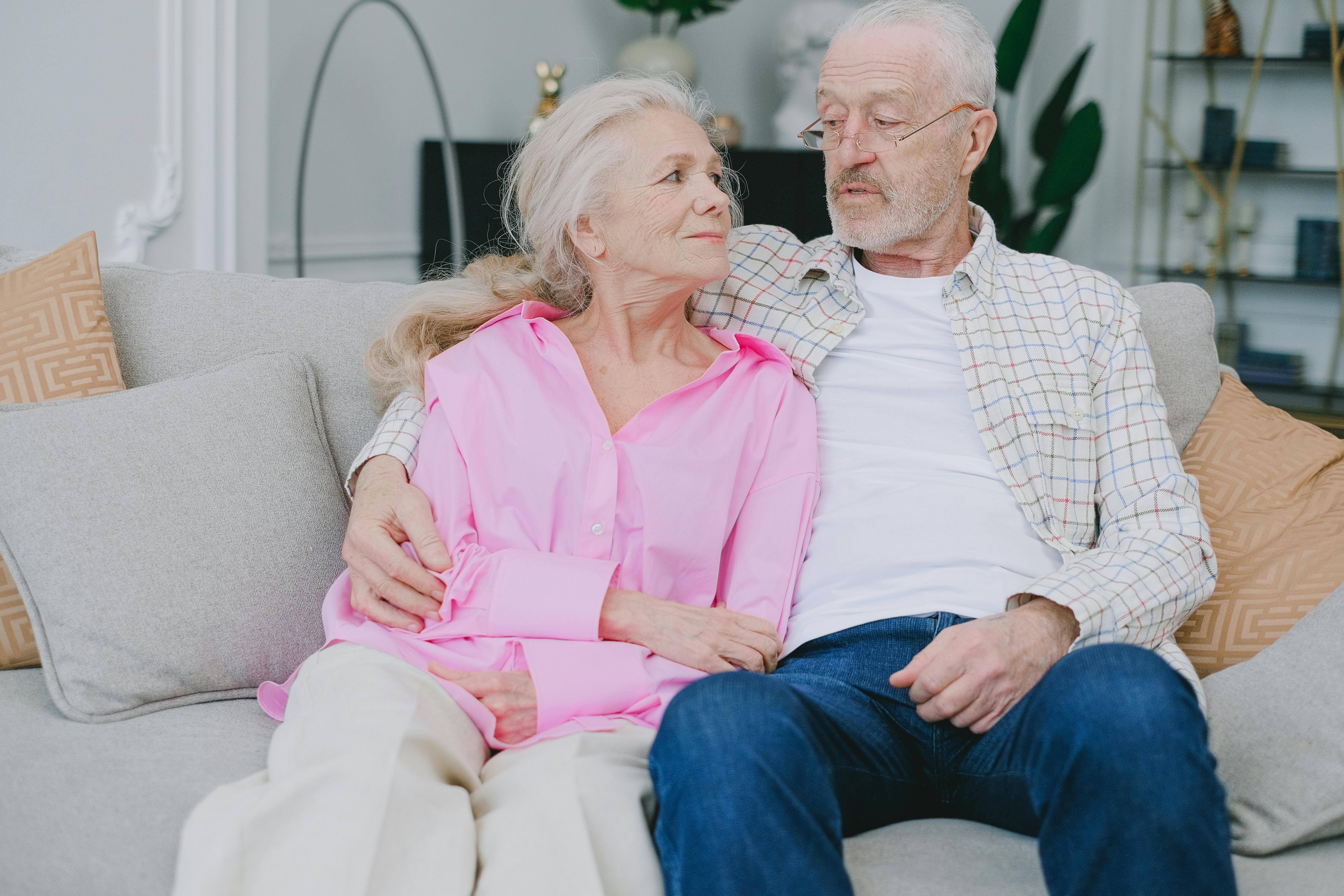 A senior couple lovingly embraces while sitting on a cozy sofa in their living room.