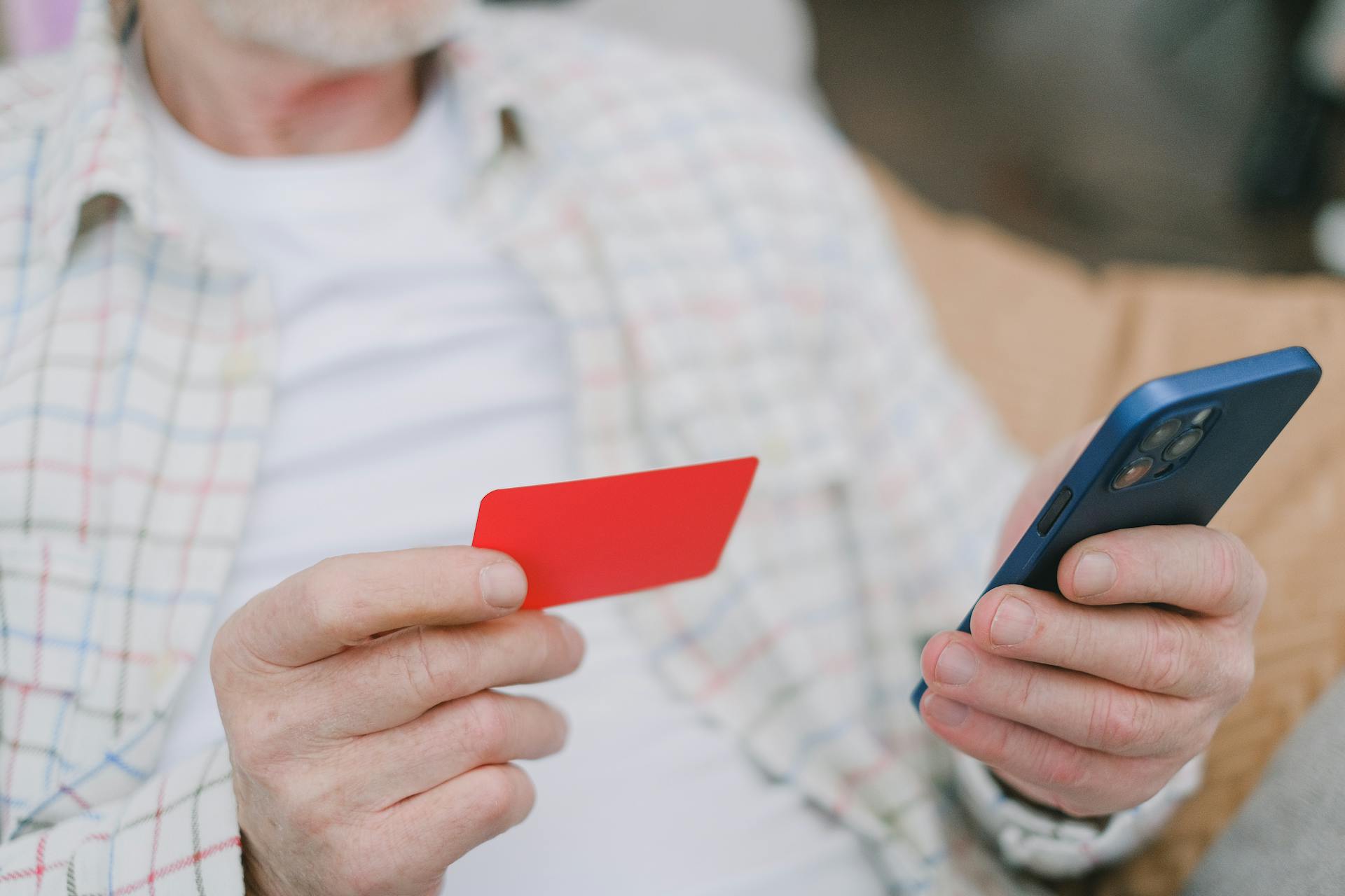 Close-up of a senior adult handling a card and smartphone for online payment.