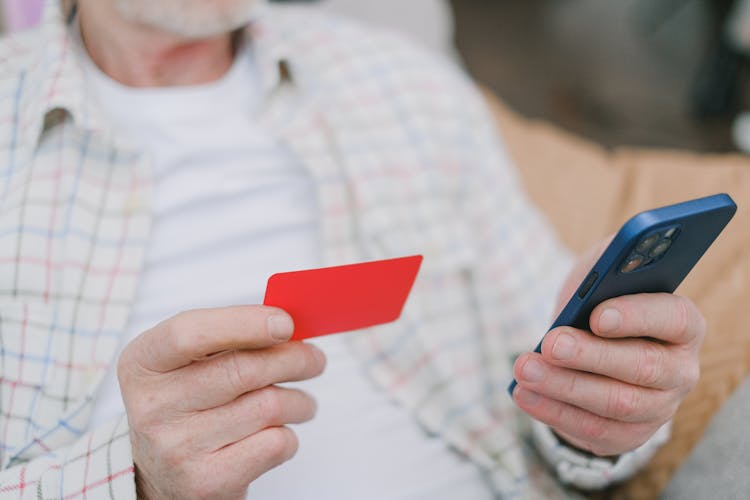 A Person's Hands Holding A Card And A Cell Phone