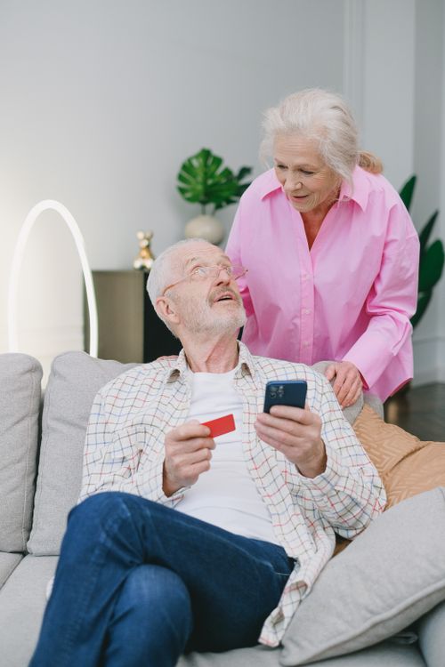 Free Elderly couple using a mobile phone and credit card for online shopping at home. Stock Photo