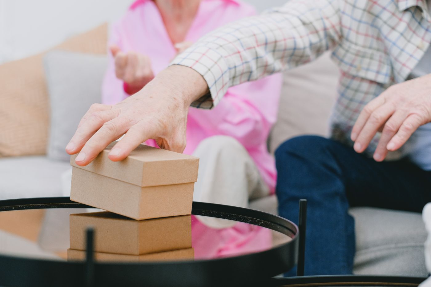 A senior man at home slowly reaching across a coffee table toward a small object