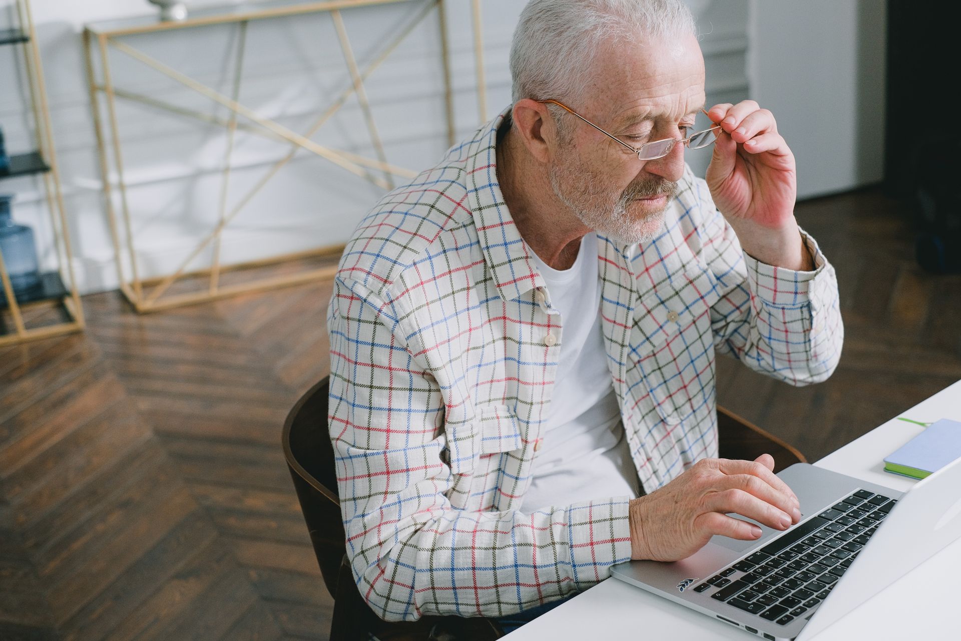 Elderly man wearing glasses focused on working at a laptop indoors.