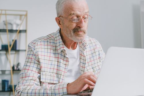 Free Senior man with eyeglasses working on a laptop in a modern indoor setting. Stock Photo