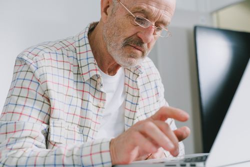 Free Elderly man in plaid shirt using a laptop indoors. Stock Photo