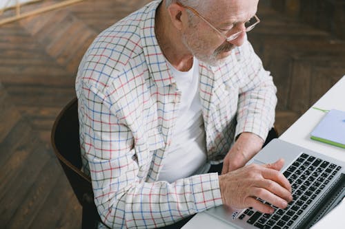 Close-Up Shot of an Elderly Man with Eyeglasses Sitting while Using a Laptop