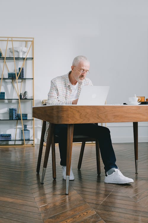 An Elderly Man with Eyeglasses Sitting while Using a Laptop