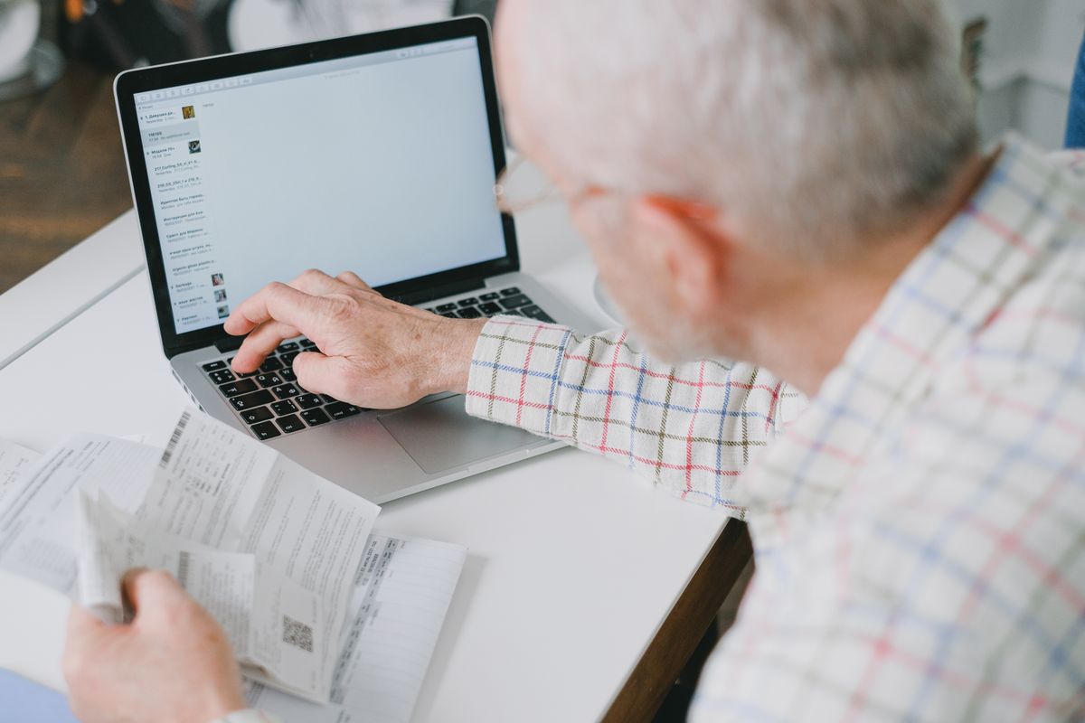 Senior man managing finances online with documents and laptop