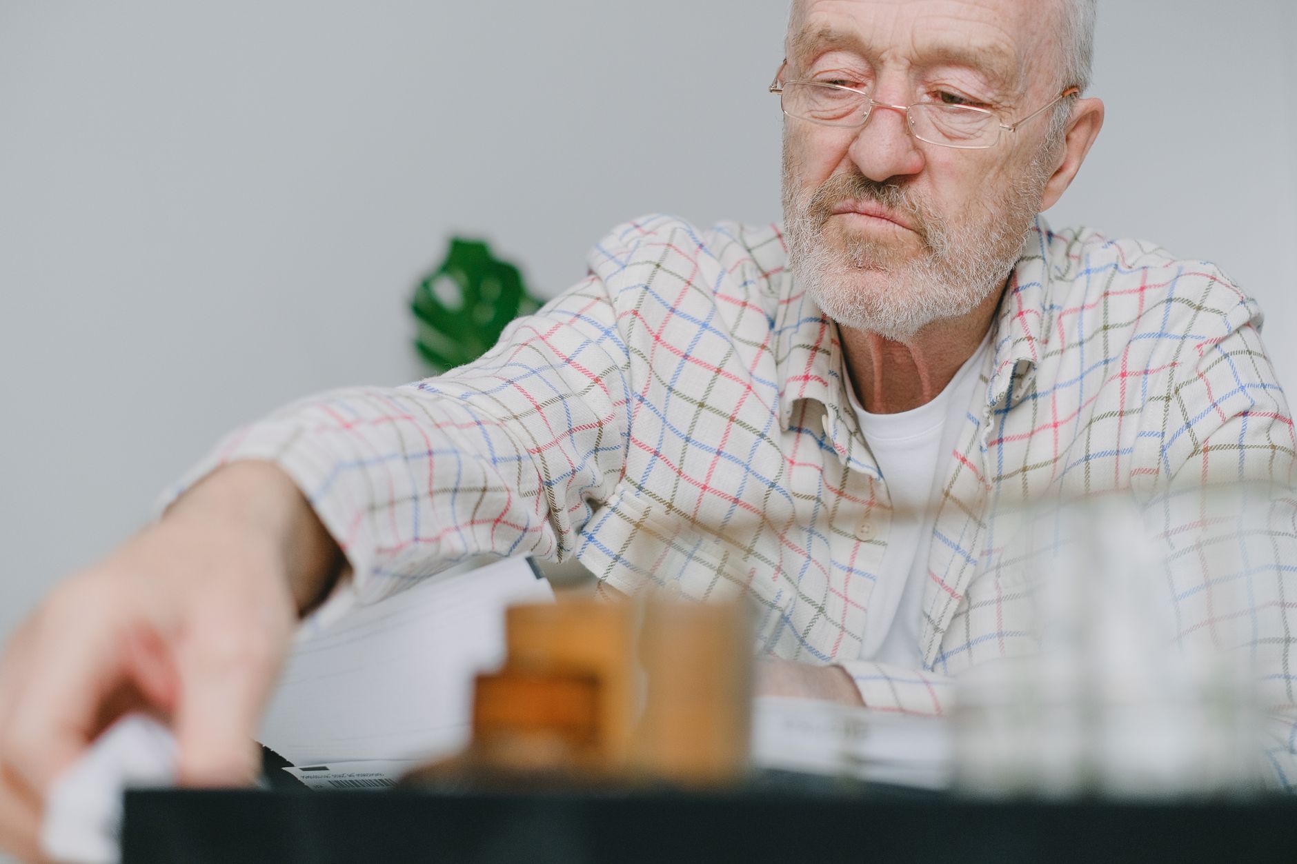 Elderly man wearing glasses, deep in thought indoors, blurred foreground.