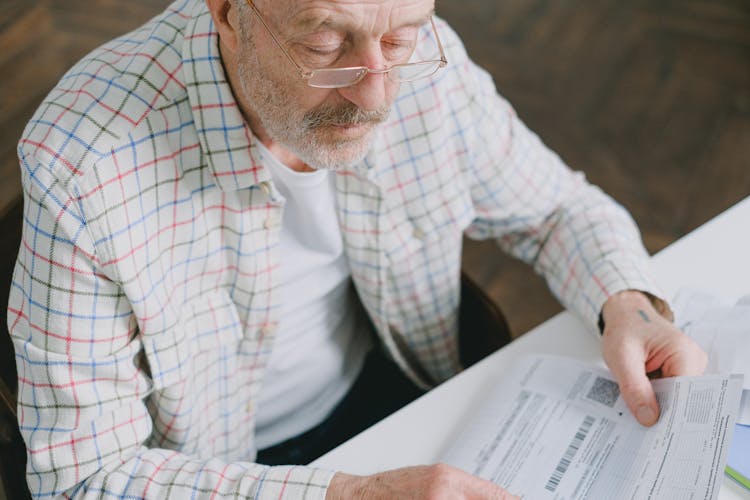 An Elderly Man Wearing Eyeglasses While Looking At The Documents