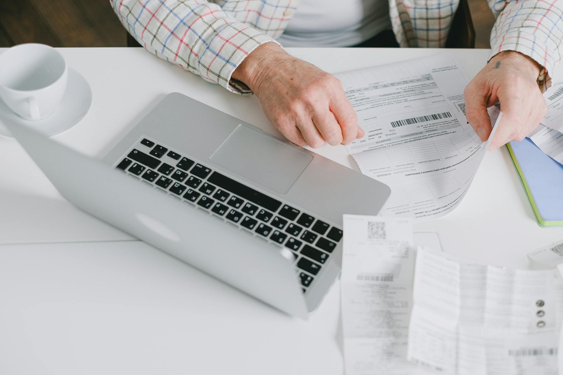 Close-up of hands organizing documents on a desk with a laptop.