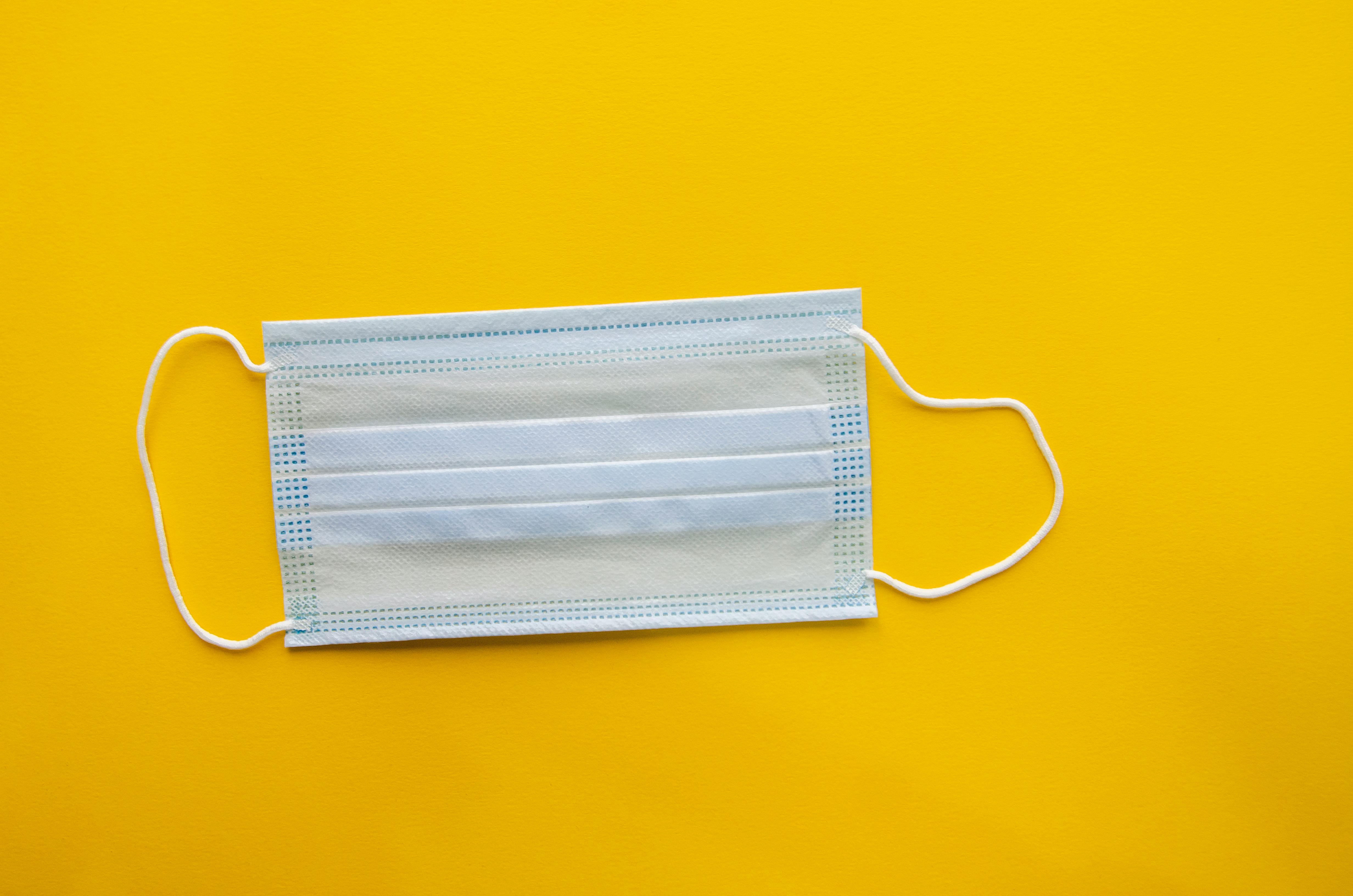 Free Close-up of a surgical face mask on a bright yellow background, ideal for healthcare concepts. Stock Photo