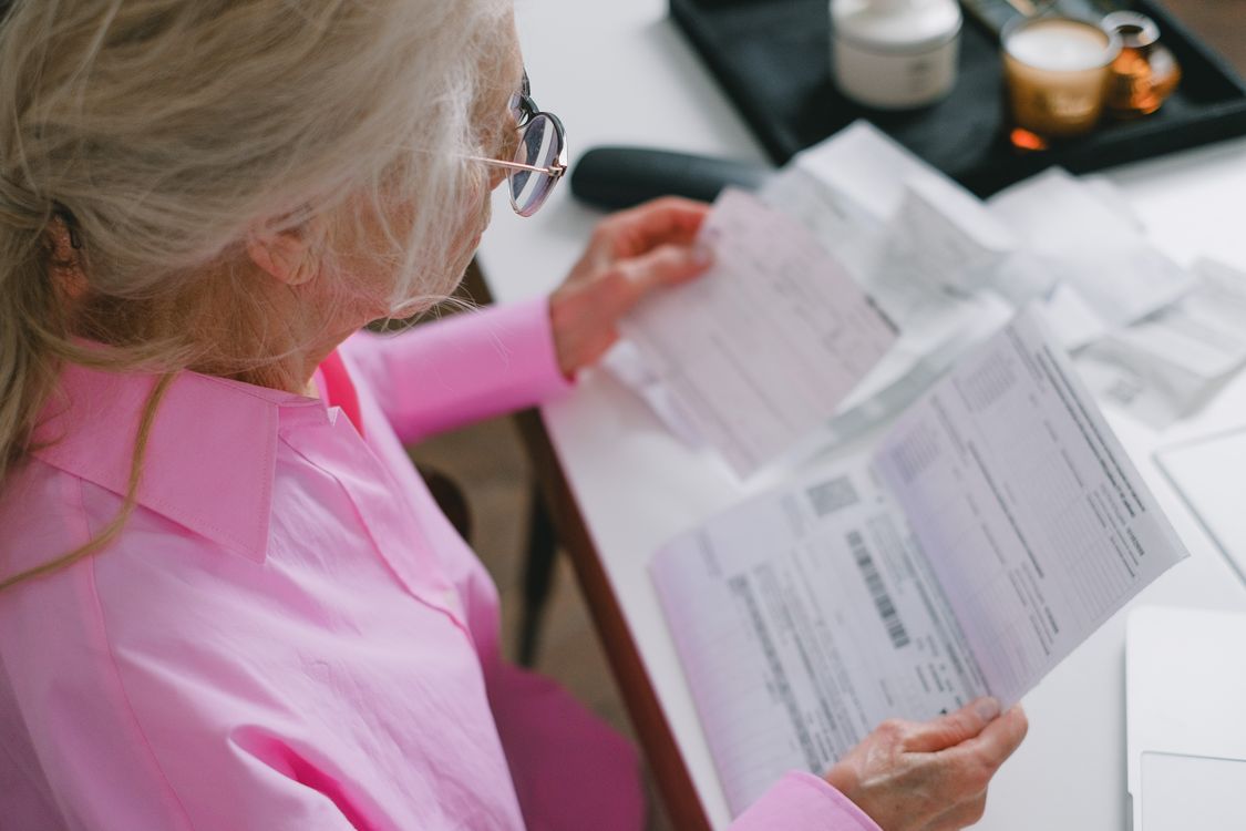 An older woman wearing glasses carefully reads important documents at a table