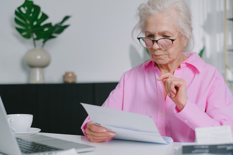 An Elderly Woman In Pink Long Sleeves Looking At Documents While Sitting