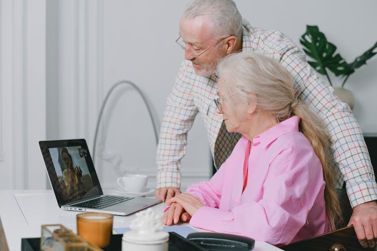 An Elderly Couple Looking At The Laptop On The Table