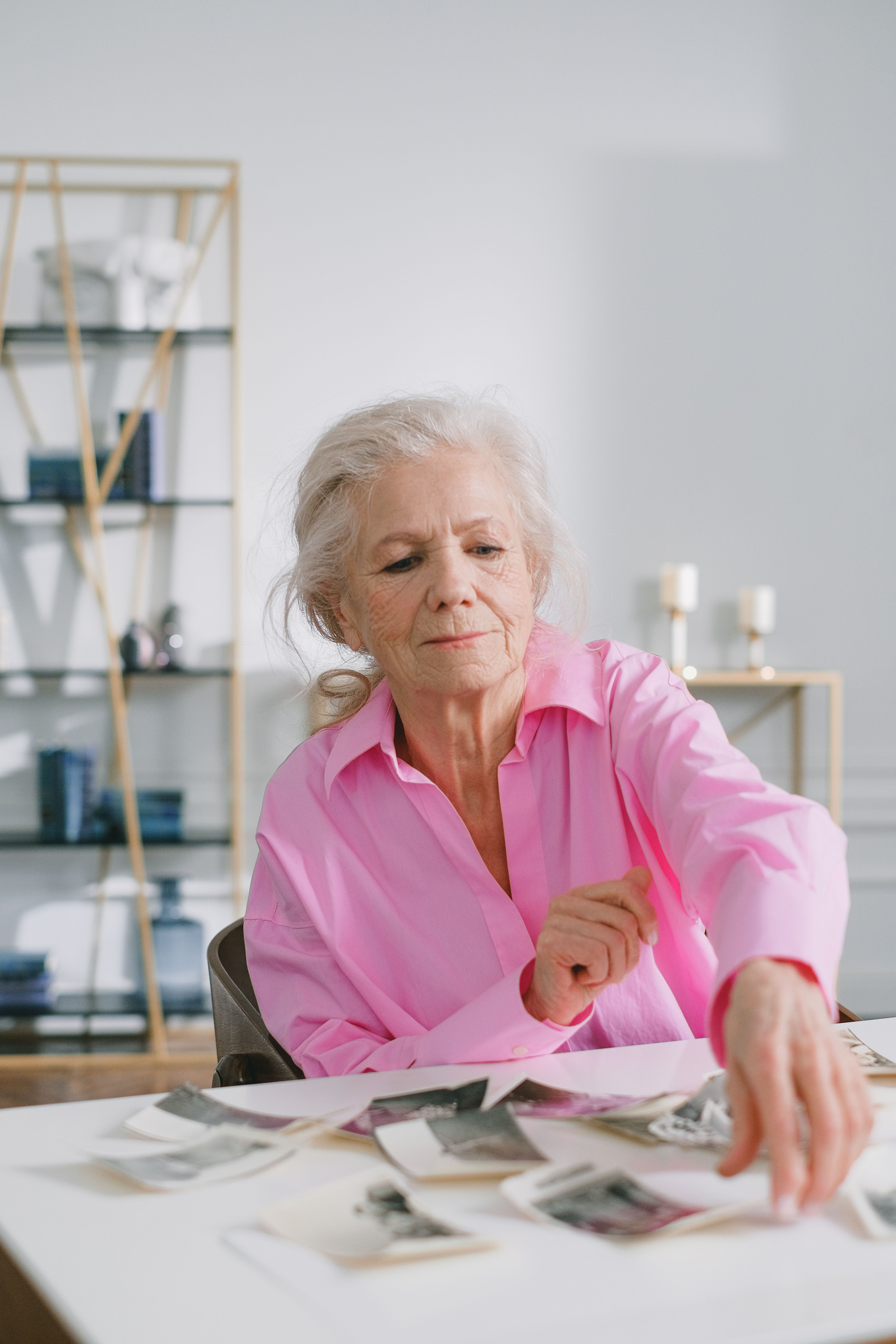 Elderly woman in pink shirt sorting vintage photographs on a table indoors.