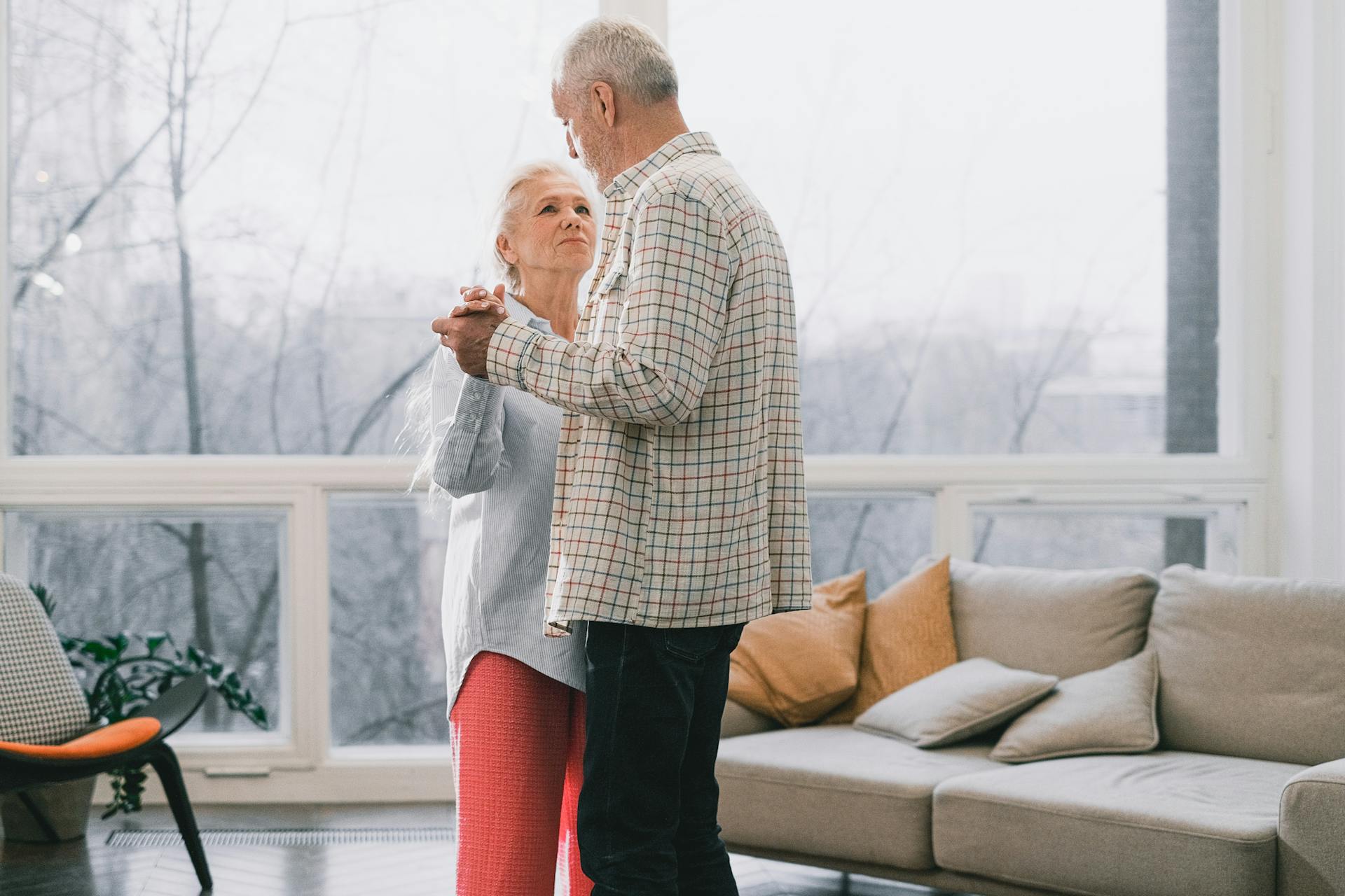 A senior couple joyfully dances together in a sunlit living room, sharing a tender moment.