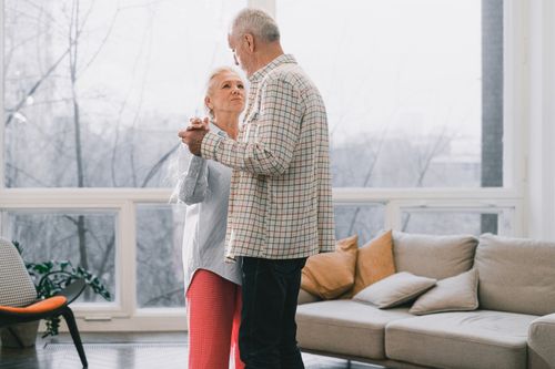 Free A senior couple joyfully dances together in a sunlit living room, sharing a tender moment. Stock Photo