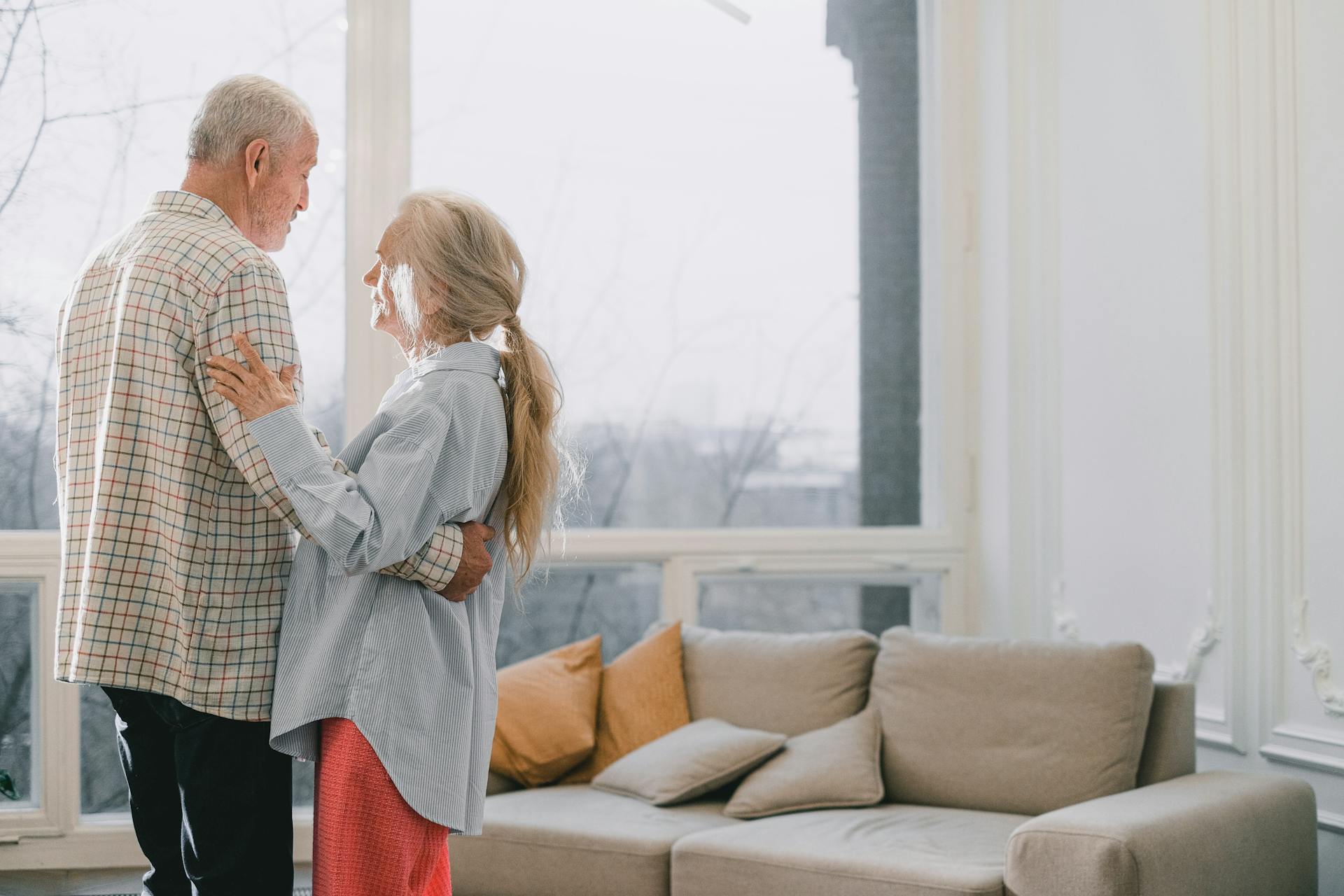 A senior couple shares a tender dance in a bright, cozy living room.