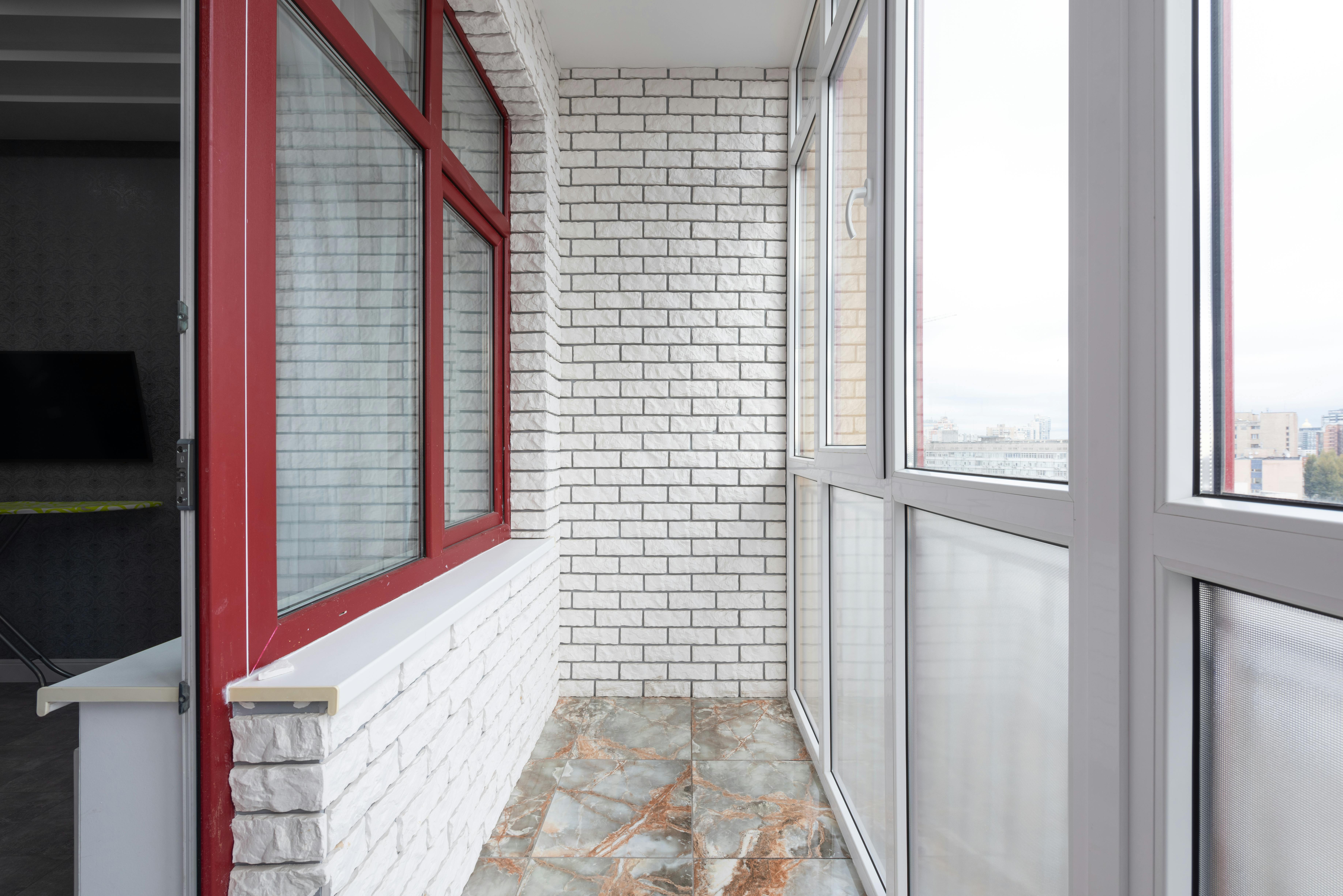 Spacious modern balcony with white brick walls and red-framed windows, capturing urban views. Best Compost Tumbler for Apartment Balcony
