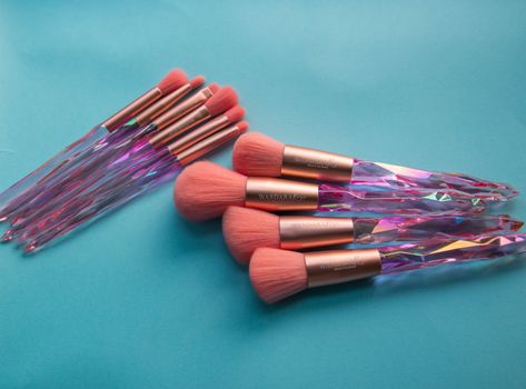 Pink and purple makeup brushes with crystal handles on blue surface. Ideal for beauty-themed content.