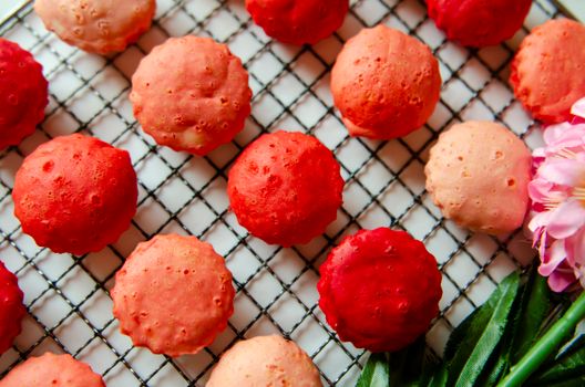 Delicious Malaysian kuih apam in vibrant red and pink hues on a cooling rack.