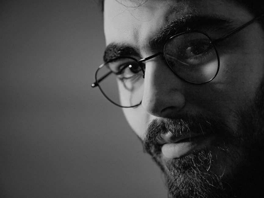 Monochrome close-up portrait of a bearded man wearing eyeglasses, with a thoughtful expression.