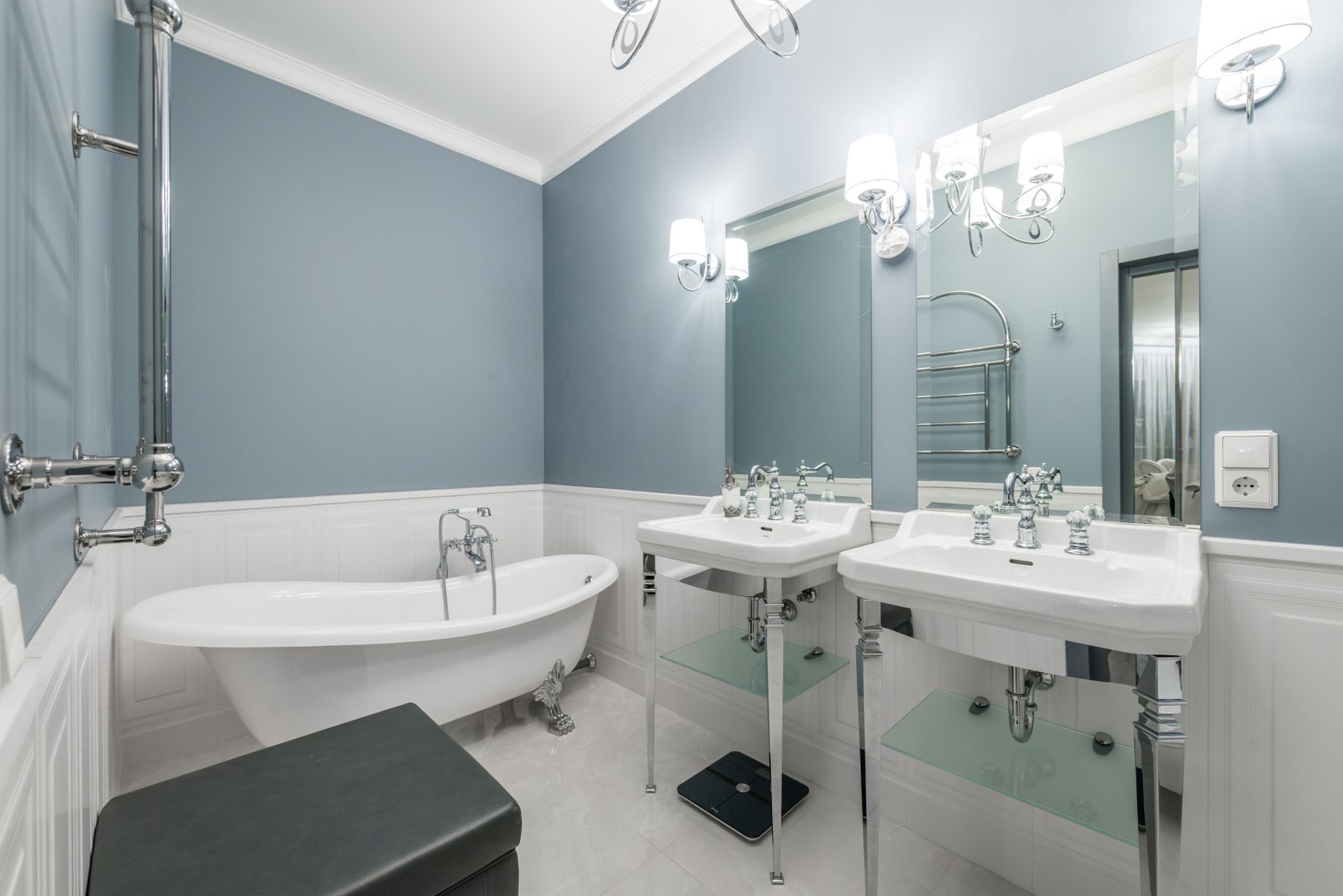 Luxury bathroom with twin sinks, mirrors, white bathtub and coordinated lighting
