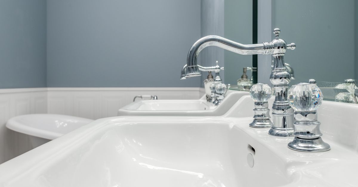 Clean white sinks with stylish metal faucets in light bathroom in luxury apartment