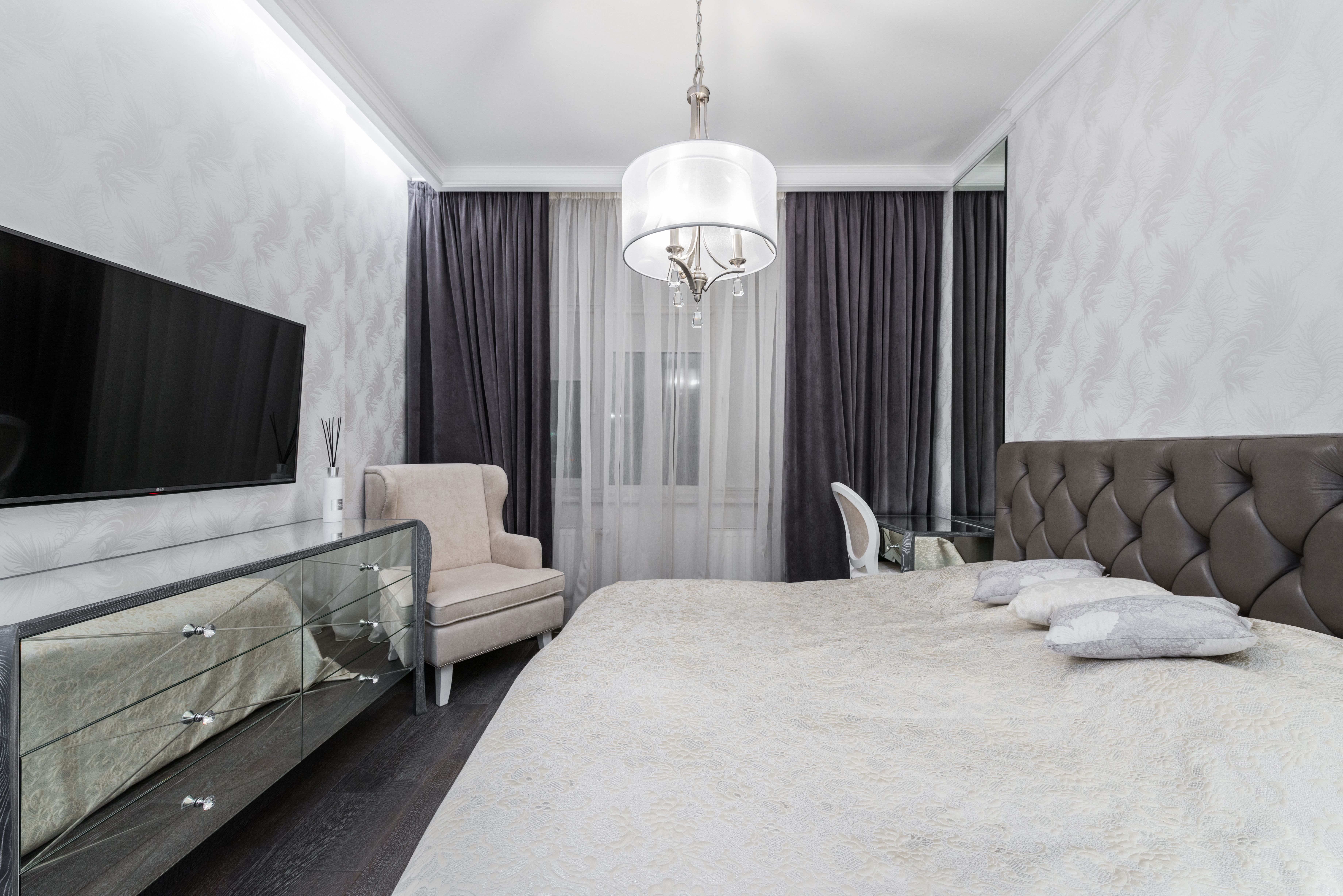 Interior of stylish bedroom with large bed with white linen placed opposite TV with black screen in luxury apartment