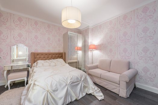 Large bed with white linen in spacious bedroom with pink furniture and walls in contemporary apartment