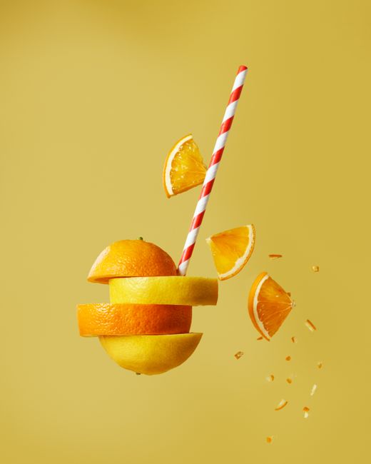 Creative photo of sliced citrus fruits with a striped straw against a yellow backdrop.