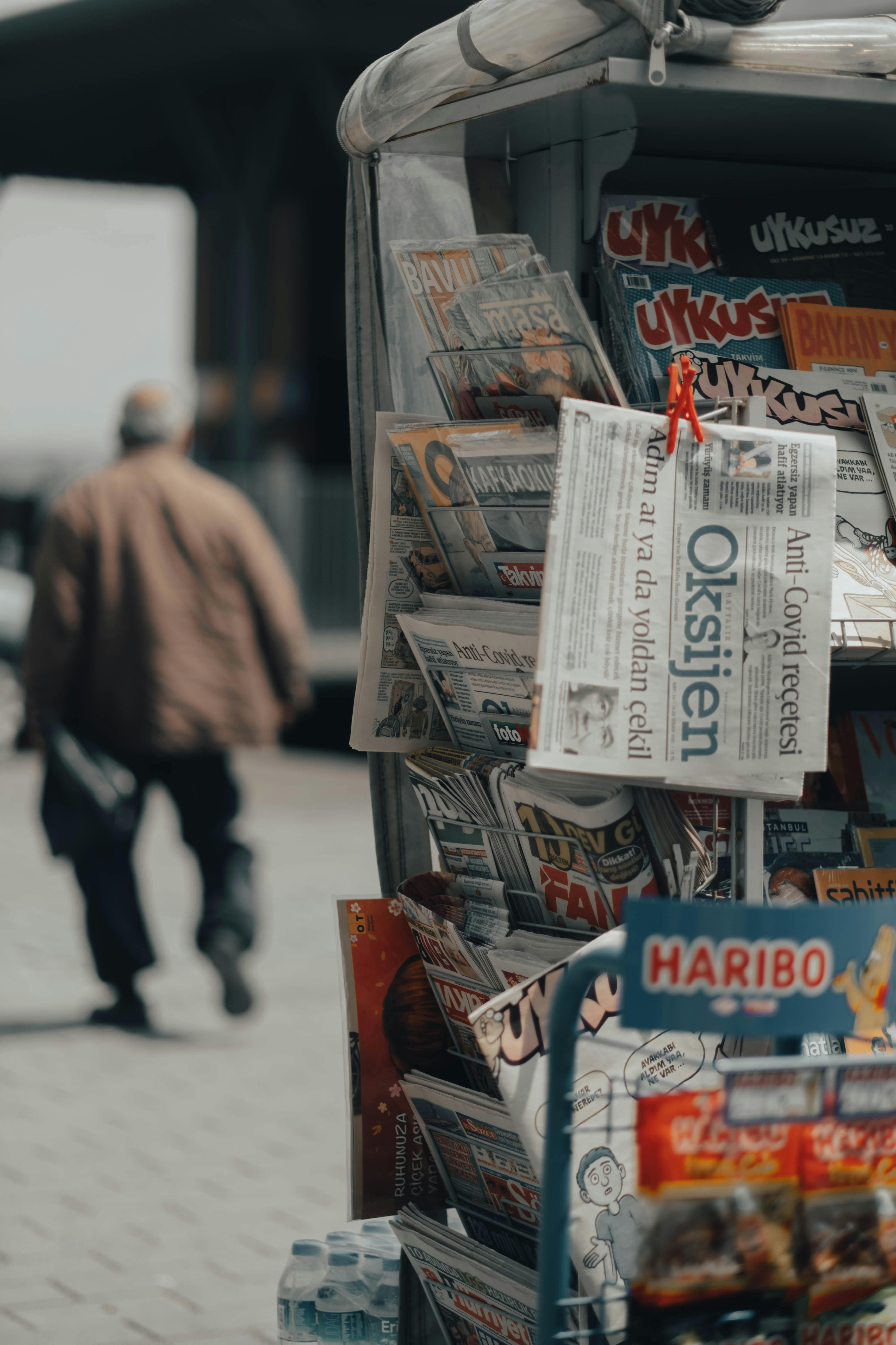 stand with newspapers in street on walkway near walking man