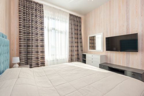 Free Contemporary bedroom with striped curtains, TV, and elegant furnishings. Stock Photo