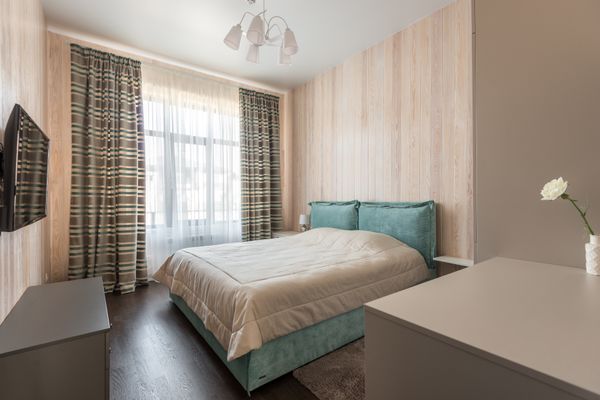 Small bedroom in pale wood with a teal bed and a curtained window — photo by Max Vakhtbovych on Pexels