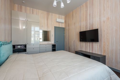 Free Contemporary bedroom featuring minimalist decor with wooden panel walls and a mounted TV. Stock Photo