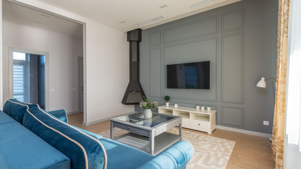 A stylish living room featuring a blue couch, wall-mounted TV, and elegant decor.