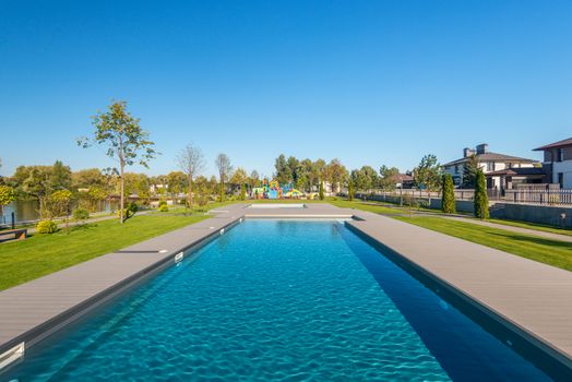 A suburban swimming pool surrounded by greenery under a clear blue sky.