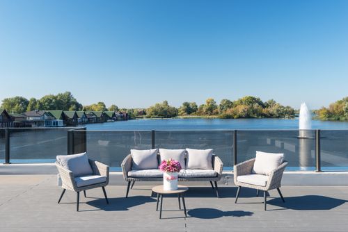 Free Modern terrace overlooking a serene waterfront with stylish furniture and vibrant flowers. Stock Photo