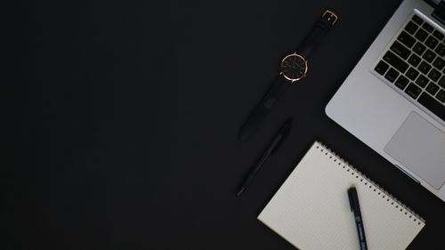 Free Top-view of a desk setup with a laptop, watch, notebook, and pens on a dark background. Stock Photo