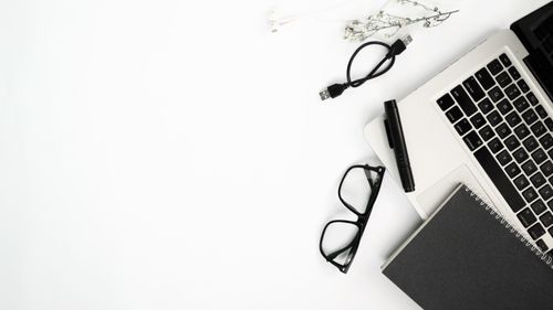 Free A minimalist flat lay of workspace essentials including a laptop, glasses, and a notebook on a white background. Stock Photo