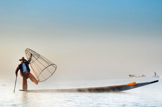 A traditional fisherman balances on a boat with a fishing net on Inle Lake, Myanmar.