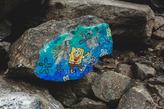 Big rock with colorful painted cartoon character placed near rough stones in daylight in countryside