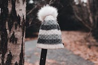 Lost and found warm knitted hat placed on metal beam near tree trunk and path with fallen dry leaves in autumn park in daytime