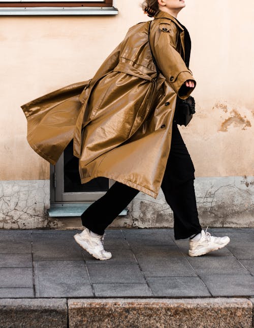 A Woman in Brown Leather Coat Walking on a Sidewalk