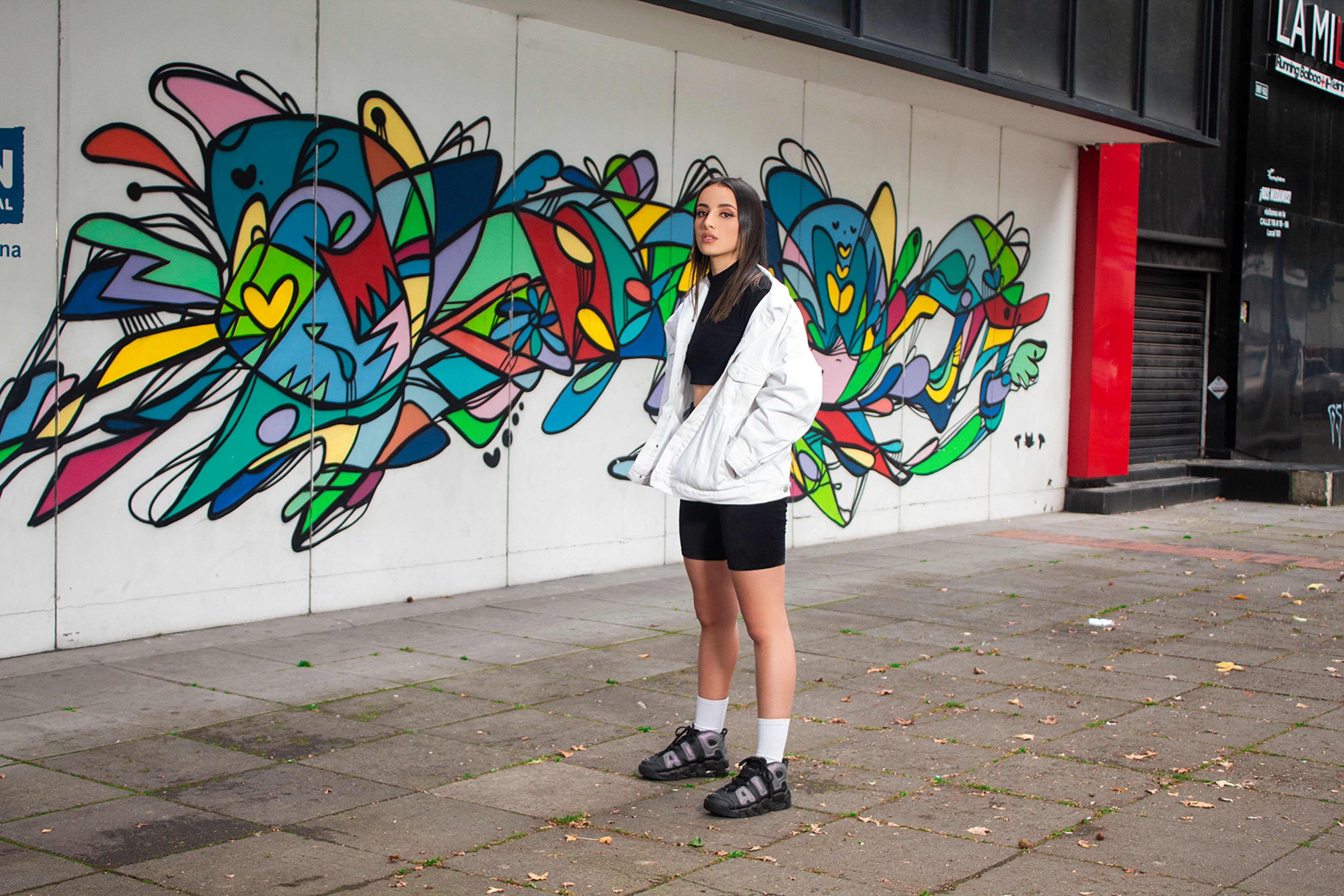 Stylish woman standing confidently by a colorful graffiti wall, showcasing urban fashion.