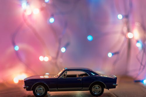 Gratis Fotografi Fokus Selektif Model Die Cast Coupe Biru Klasik Di Depan Lampu String Di Atas Meja Foto Stok