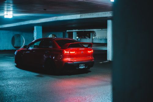 Free A red Mitsubishi Lancer Evo parked inside a dimly lit parking garage, showcasing its sporty design. Stock Photo
