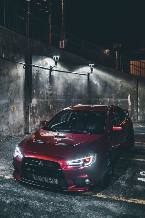 Free A red Mitsubishi Lancer Evo parked in a dimly lit urban area at night, highlighting its sleek design. Stock Photo
