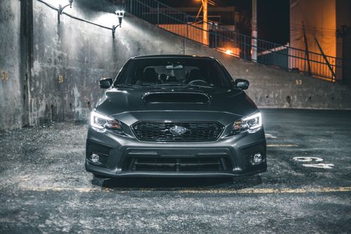 Free Front view of a gray Subaru WRX parked in a dimly lit urban parking area at night. Stock Photo